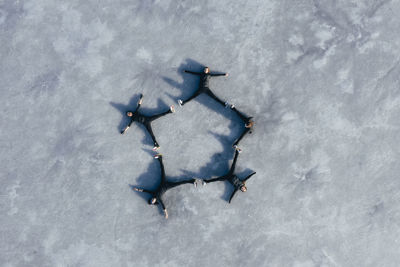 Aerial view of group of female ice-skaters lying together on surface of frozen lake