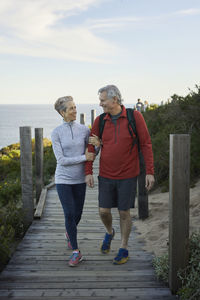 Full length of couple waling on boardwalk against sky