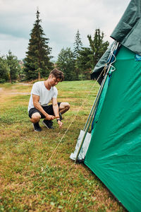 Young man putting up a tent on camping during summer vacation trip. teenager putting the stakes