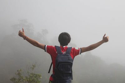 Rear view of boy standing in foggy weather against sky