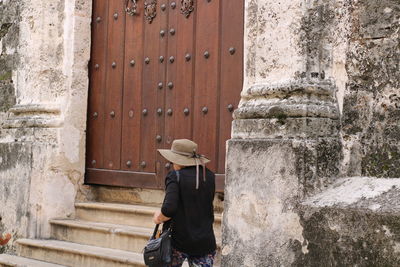 Rear view of woman wearing sun hat while walking by old building