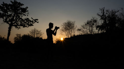 Silhouette man standing on field against sky during sunset