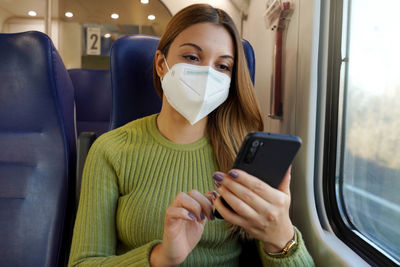 Relaxed woman on train wearing medical face mask using smart phone app