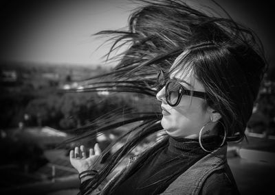 Close-up of young woman tossing hair against sky