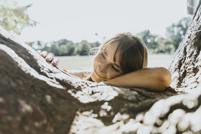 Smiling mature woman with head on tree trunk in public park