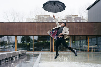 Man jumping on wet umbrella during rainy season
