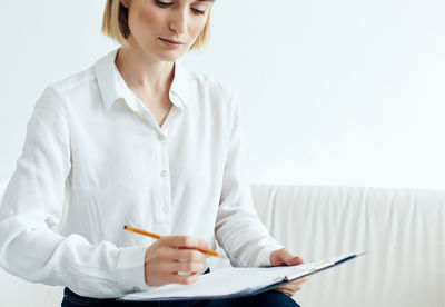 Midsection of a young woman sitting on table against white background
