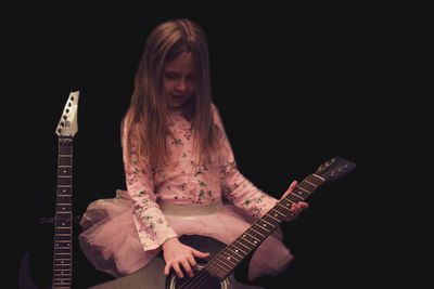 Young woman playing guitar against black background