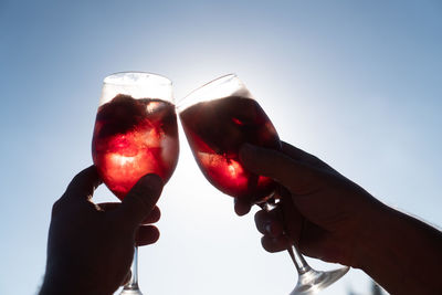 Low angle view of hand holding drink against sky