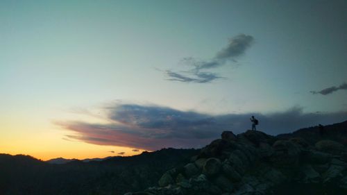 Silhouette man standing on rock against sky during sunset