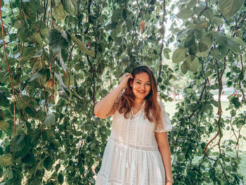 Portrait of smiling young woman standing against trees