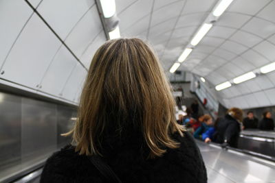 Rear view of woman standing on escalator at illuminated subway station