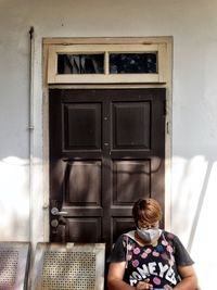 Mature woman wearing mask sitting by door outdoors