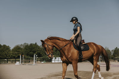 Woman horse riding on paddock at sunny day