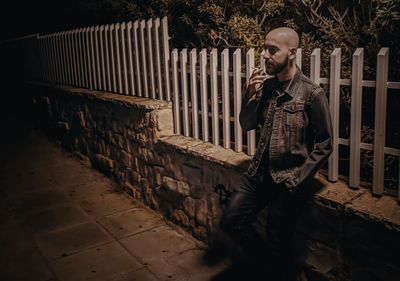 Young man looking away while standing against brick wall