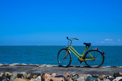 Bicycle on rock by sea against blue sky