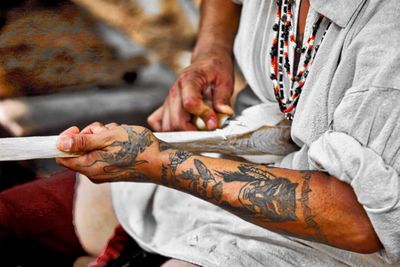 Midsection of man carving wood while sitting outdoors