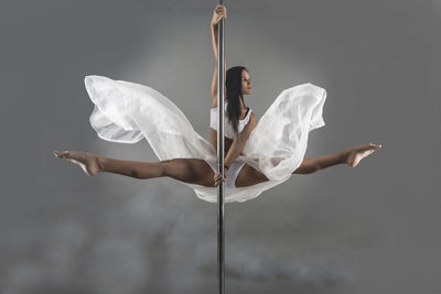 Young pole dancer performing against gray background