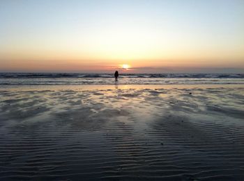 Silhouette man standing on beach against clear sky during sunset