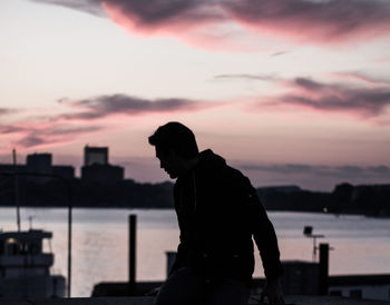 Silhouette man with railing against sky during sunset