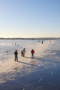 People on beach against clear sky during winter