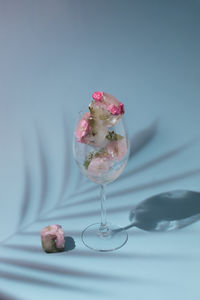 Small pink flowers in transparent glass on blue background with copy space. sunny day concept