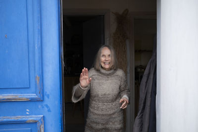 Smiling senior woman standing in doorway and waving