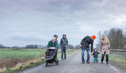 Family walking on road against cloudy sky during winter