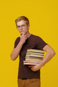 Portrait of young woman holding book against yellow background