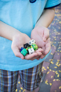 High angle midsection of boy holding various dices while standing on footpath
