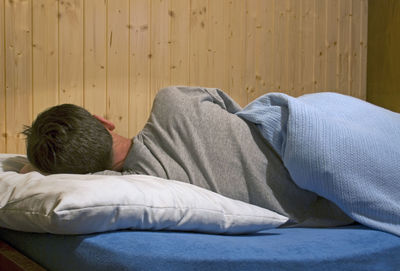 Rear view of man sleeping on bed at home