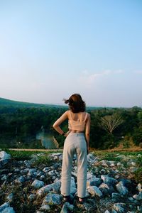 Rear view of woman standing on rock against sky