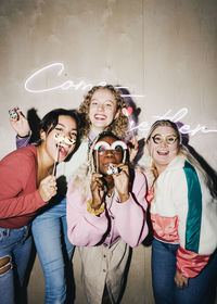 Portrait of cheerful multiracial female roommates with props against wall in college dorm