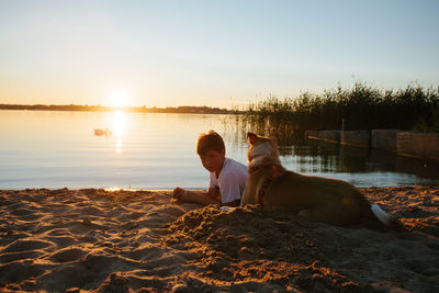 Woman with dog on beach against sky during sunset