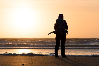 Rear view of man standing at beach during sunset