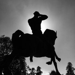 Low angle view of silhouette man riding statue against sky