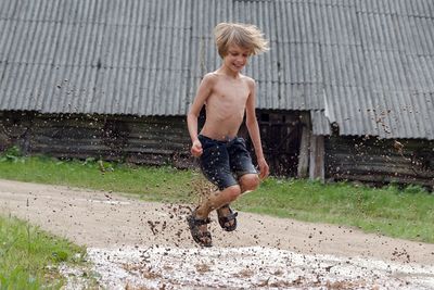 Full length of shirtless boy jumping over muddy puddle