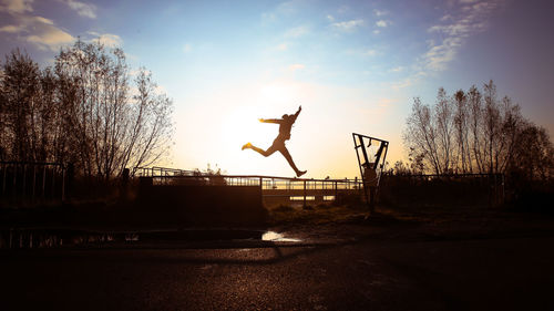 Silhouette man jumping against sky at sunset