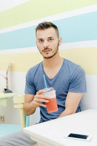 Portrait of a young man drinking glass on table