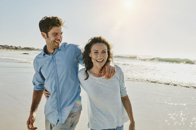 Happy friends standing on beach against sky