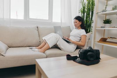 Young woman using laptop while sitting on sofa at home