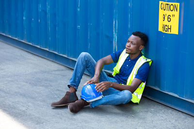 Full length of smiling young woman sitting against blue wall