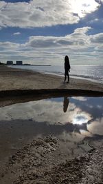 Silhouette woman walking on beach against sky during sunset