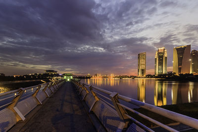 River by illuminated city against sky at sunset