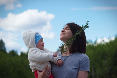 Low angle view of smiling mother carrying cute daughter while standing against sky