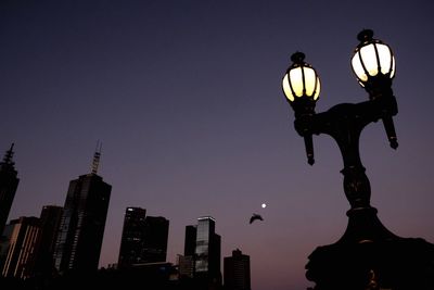 Low angle view of illuminated street light by modern buildings at dusk