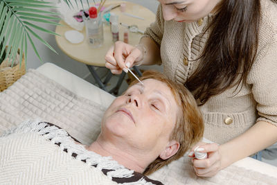 A cosmetologist paints the eyebrows of an elderly woman.