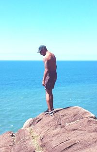 Man standing on rock looking at sea against sky