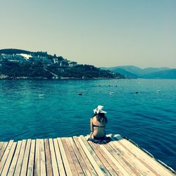 Man sitting on pier over sea against clear sky