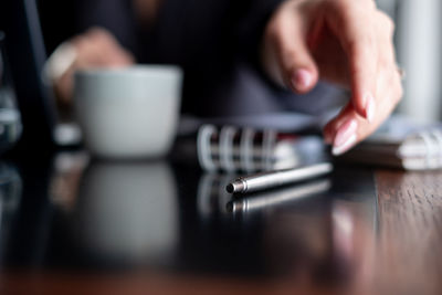 Close-up of businesswoman picking pen on table